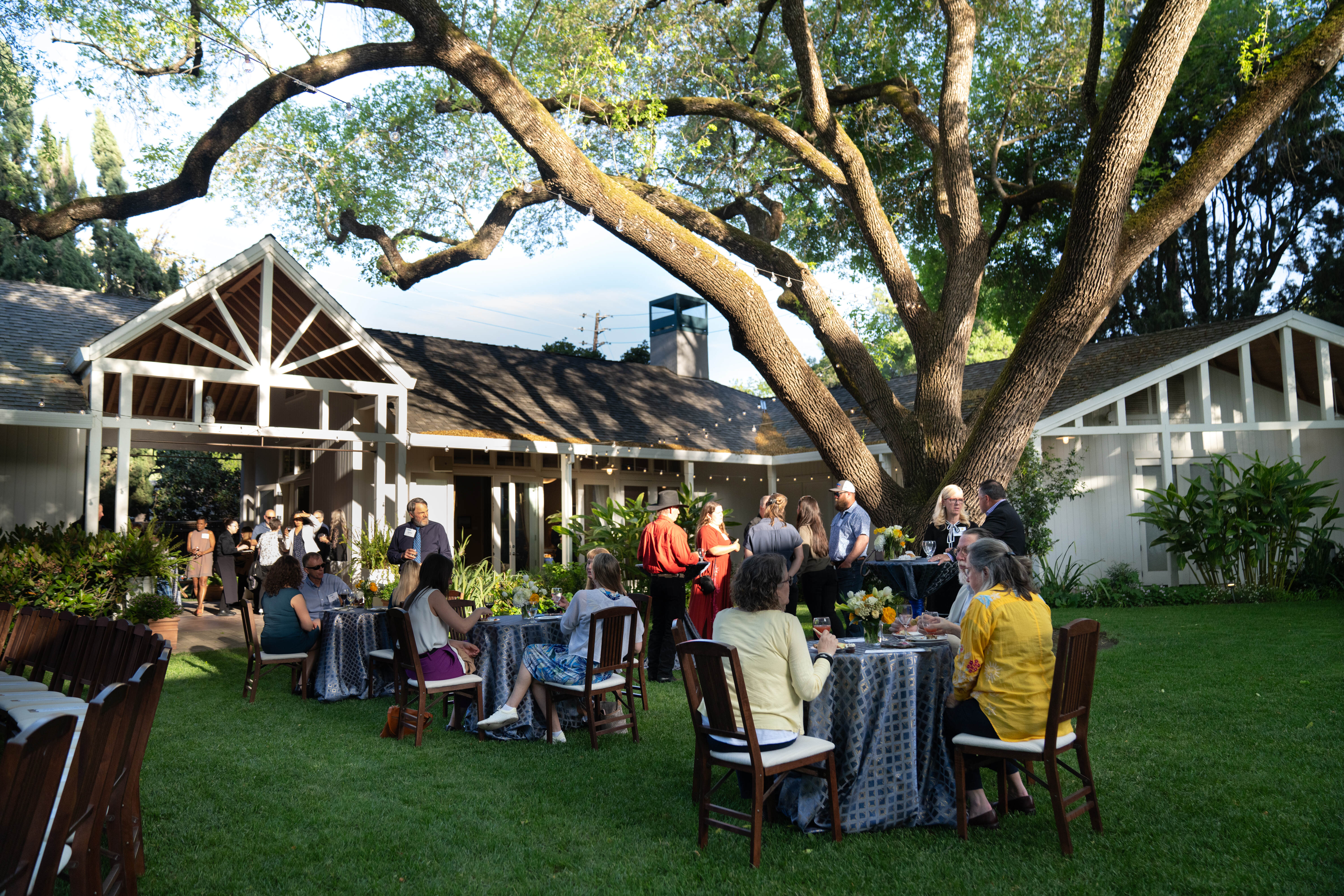 People sitting at tables and standing in the courtyard, talking.
